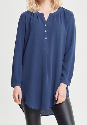 Námořnicky modrý dlouhý rukáv tunika s kulatým výstřihem a tříknoflíkovou légou. Měkká, lehká tkanina s mírně delším zadním dílem.