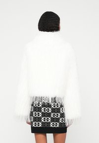 Bela puhasta krojena jakna z visokim ovratnikom, v kombinaciji s tesnim črnim krilom, ki ima bel geometrijski vzorec. Gladka tekstura.