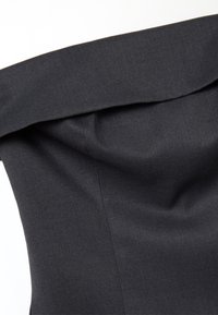 Primo piano di un tessuto nero con colletto piegato e cuciture visibili, che mostrano la texture e i dettagli delle cuciture su misura.