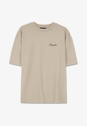 Beige bavlněné tričko s volným střihem, krátkými rukávy a malým černým logem "Pegador" na levé hrudi. Hladká textura, kulatý výstřih.