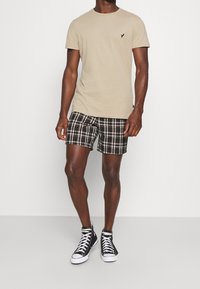 Beige cotton t-shirt with a small black logo, paired with black and white plaid shorts and black high-top sneakers with white soles.
