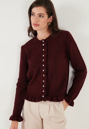Burgundy cardigan with ruffled edge, button closure, long sleeves, and textured knit material. Features small white buttons along the front.