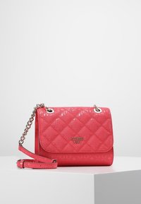 Růžová prošívaná kabelka z lakované kůže se stříbrným řetízkovým popruhem a logovými doplňky. Má klopnové zapínání s označením značky.