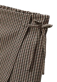 Gros plan sur une jupe en motif pied-de-poule brun et beige avec une ceinture élastique et une ceinture en tissu nouée.