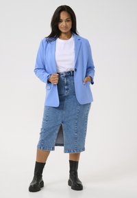 Blazer azul claro sobre una camiseta blanca, combinado con una falda lápiz de mezclilla con una abertura delantera. Botines negros completan el atuendo.