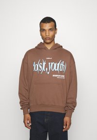 Brun huvtröja med ett stort blått grafiskt tryck som läser "do(s)t, you(th)" och "säsong ett" på framsidan. Har en känguruficka och dragsko i huvan.