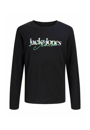 Jongen met een grijze pet, zwarte spijkerjas en broek, zwart T-shirt met print en bruine leren schoenen, staand iets naar rechts gericht.