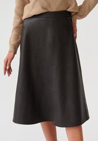 Jupe midi en cuir noir avec une texture lisse, un design évasé et une taille ajustée, associée à un pull en tricot beige clair.