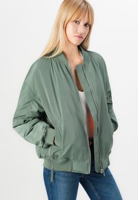 Green bomber jacket in lightweight material with a zip front, ribbed cuffs, and side pockets; features smooth texture and slightly loose fit.