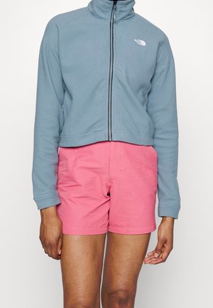 Veste en polaire courte bleu clair avec un col haut et une fermeture éclair. Associée à un short rose. Les deux vêtements présentent une coupe décontractée.