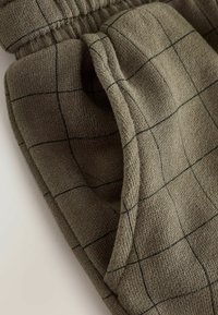 Pantaloni sportivi verde a scacchi con vita elasticizzata e tasca laterale, che mostrano una texture morbida e un design loose fit.