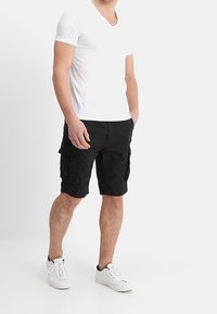 Pantalones cortos cargo negros con múltiples bolsillos, hechos de una tela duradera. Combinados con una camiseta blanca de cuello en V y zapatillas blancas.