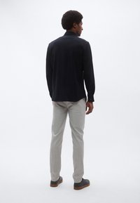 Granatowa koszula z długim rękawem o prostym obszyciu, zestawiona z jasnoszarymi, dopasowanymi spodniami i ciemnym obuwiem, widziana od tyłu.