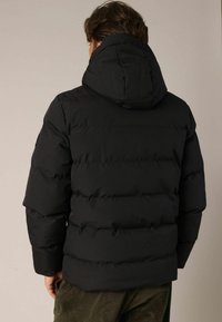 Veste matelassée noire avec capuche, dotée d'un design en quilting et d'une isolation épaisse. Le tissu semble lisse et mat. Aucune pièce métallique visible.