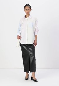 Button-up shirt in pale pink and blue stripes, paired with a black leather pencil skirt featuring a front slit. Model holds a cream-colored bag.
