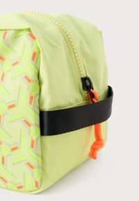 Limoengroene ritszak gemaakt van gestructureerd nylon, met een geometrisch patroon in fluorescerende kleuren, een zwarte strap en een oranje trekhaak.