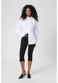 White button-up shirt featuring a collar, paired with black cropped pants and black heeled shoes. Smooth fabric and classic design.