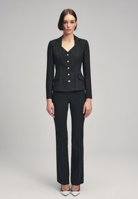 Zwarte op maat gemaakte blazer met vijf gouden knopen, twee voorzakken en strakke revers, gecombineerd met aansluitende zwarte broek. Glad textuur overal.