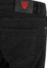 Mustad denim teksad, millel on tekstureeritud viimistlus. Omab tagakotti ja punast logo plaati vöökohal. Lihtne ja funktsionaalne disain.