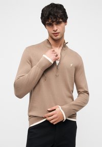 Pull-over marron en tricot avec col à fermeture éclair partielle, présentant des accents blancs aux poignets et à l'ourlet. Coupe ajustée, texture douce, marquage minimaliste sur la poitrine.