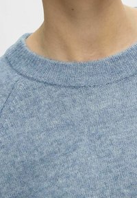 Vaaleansininen neulottu neulepaita, jossa on resorireunainen pyöreä kaulus, pehmeä rakenne ja hienovarainen kuvio koko kankaassa.