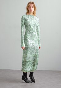 Grön långärmad klänning med texturerat, quiltat mönster. Inskuren silhuett, knälång, kombinerad med svarta ankelskor. Slät, glänsande tyg.