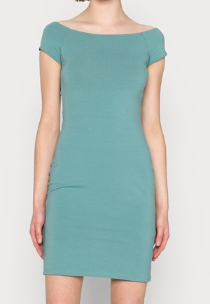 Robe courte ajustée à manches courtes de couleur sarcelle avec un large décolleté bateau, portée par une personne debout devant un fond uni.