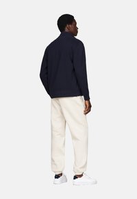 Chaqueta de punto azul marino, pantalones de chándal beige, zapatillas blancas. La chaqueta presenta un collar y puños acanalados; los pantalones de chándal tienen tobillos elásticos y bolsillos laterales.