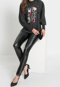 Jersey gris con estampado festivo, pantalones negros de cuero sintético y tacones negros de punta. Material texturizado, corte relajado y bolso con cadena.