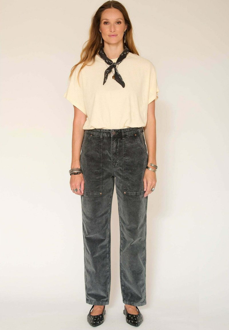 Pantalon en velours côtelé gris avec poches latérales et fermeture à bouton, associé à un t-shirt oversize crème et une écharpe noire à motifs. Ballerines noires.