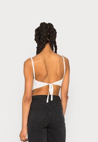Top cropped branco com alças finas, tecido texturizado, design com laço nas costas. Combinado com jeans pretos de cintura alta com bolsos traseiros.