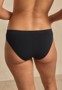 Culotte noire à texture lisse et design classique, présentant une coupe haute au niveau des jambes et une ceinture douce et élastique.