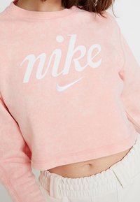Rosa kortärmad sweatshirt av mjukt material, med en vit "Nike"-logotyp och en liten swoosh, rund halsringning och ribbade ärmmuddar.