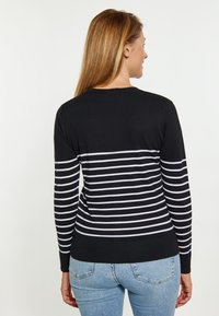 Maglione a righe bianco e nero con maniche lunghe e polsini a costine. Tessuto morbido, design aderente. Indossato con jeans azzurri chiari.