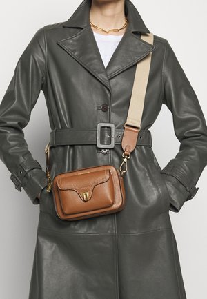 Borsa a tracolla in pelle marrone con finiture dorate e superficie testurizzata, dotata di chiusura a patta e tracolla regolabile, indossata sopra un cappotto in pelle grigia.