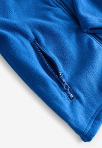 Giacca in fleece blu con una texture liscia e una tasca con zip. Presenta una zip blu coordinata, mostrando un design funzionale.