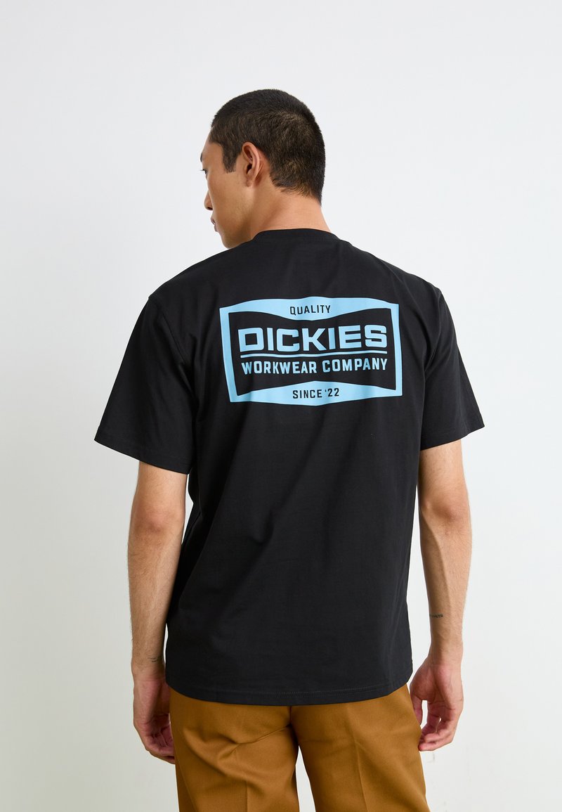 Svart bomullst-skjorte med korte ermer, med stor blå grafikktrykk på baksiden som viser "DICKIES WORKWEAR COMPANY" og "KVALITET."