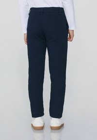 Granatowe spodnie wykonane z tkaniny o splocie, charakteryzujące się prostym krojem, pętelkami na pasek i kieszeniami, zestawione z białymi trampkami i białą bluzką.