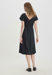 Schwarzes, knielanges Kleid mit kurzen Ärmeln und V-Ausschnitt auf der Rückseite. Verfügt über einen elastischen Taillenbund für eine taillierte Silhouette und eine glatte Stofftextur.