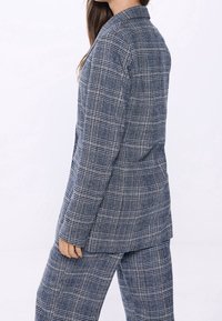 Traje de cuadros azul marino que incluye un blazer largo y entallado y pantalones de pierna ancha, confeccionado con una tela texturizada con líneas contrastantes en blanco y azul.