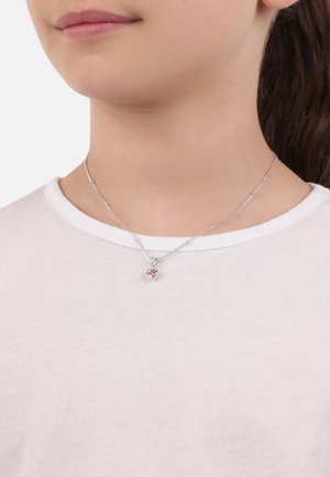 Silberne Kettenhalskette mit einem kleinen rosa Herzanhänger. Die Trägerin trägt ein einfaches weißes Shirt mit glatter Textur und rundem Ausschnitt.