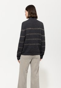 Dunkelgrauer gestrickter Pullover mit hohem Kragen. Verfügt über vertikale Streifen aus helleren Fäden und lange Ärmel. Getragen mit beigen weit geschnittenen Hosen.