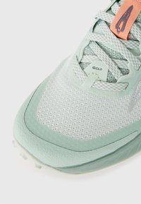 Light green athletic shoe with mesh upper, rounded toe, textured rubber sole, and a peach accent on the tongue. Features laces and branding.