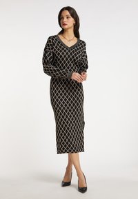 Musta pitkähihaisuus mekko V-kaula-aukolla, jossa on beige timanttikuosi. Valmistettu pehmeästä kankaasta, siinä on vartalonmyötäinen leikkaus ja ribattu hihansuu.
