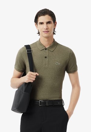 Polo de color verde oliva con cuello, dos botones y un pequeño logo. Combinado con pantalones negros y un bolso negro texturizado.