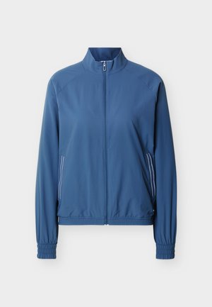 Chaqueta azul con cremallera, cuello alto, puños elásticos y dos bolsillos laterales con cremallera que presentan rayas verticales blancas.