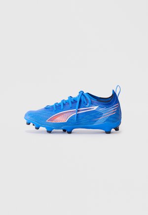 Botín de fútbol azul con detalles en naranja y blanco, cordones atados y tacos negros en la suela, aislado sobre un fondo blanco.