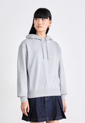 Felpa grigia chiara e corta con cappuccio regolabile e orlo a coste. Abbinata a una gonna di jeans scura con cuciture visibili.