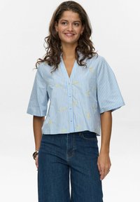 Lichtblauw cropped shirt met verticale gele strepen en bloemenbroderie. Loose fit met korte mouwen en knoopsluiting.