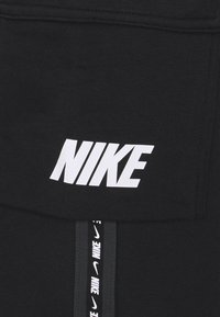 Svart tyg med en stor vit "NIKE"-logotyp och en vertikal rand med upprepade "NIKE"-märkningar i vitt. Slät textur, sportig design.